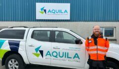 A man in a high-visibility vest standing next to a white pickup truck with the aquila waste management solutions logo.