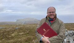 A man holding a red book on top of a mountain.