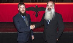 Two men shaking hands in front of a red curtain.