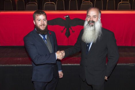 Two men shaking hands in front of a red curtain.