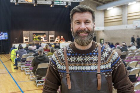 A bearded man in an apron standing in an auditorium.