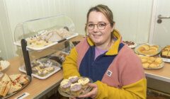 Woman presenting cupcakes at a bakery stand.