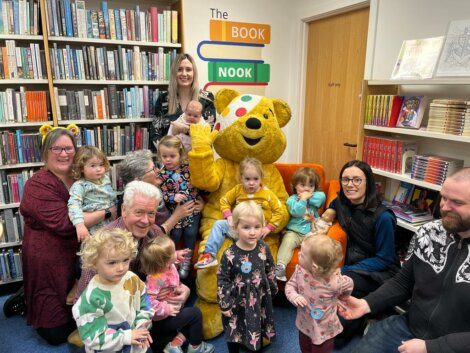 A group of children posing with a teddy bear in a library.