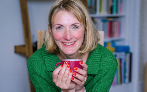 A woman holding a red mug in front of a bookcase.