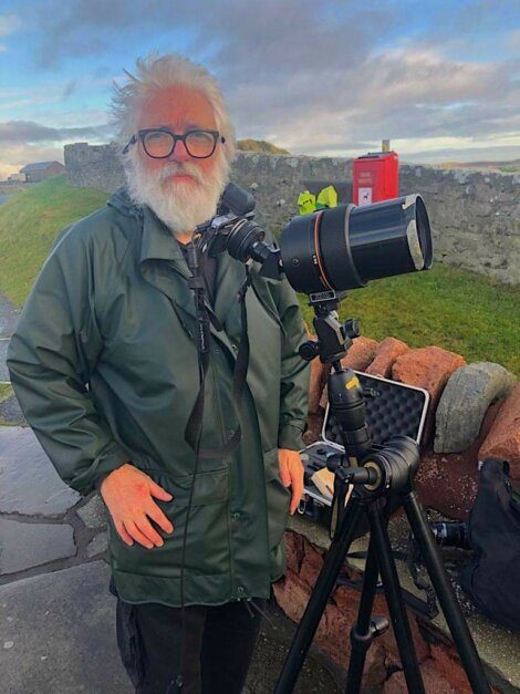 A man standing next to a tripod with a camera.