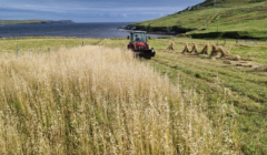 A tractor driving through a field near the ocean.