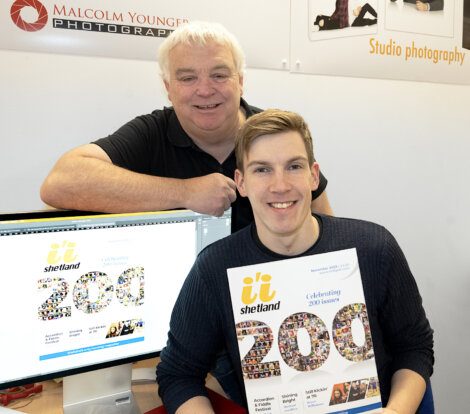 Two men posing for a photo in front of a computer.