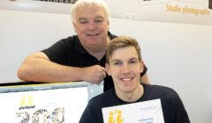 Two men posing in front of a computer.