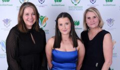 Three women posing for a photo in front of a green wall.