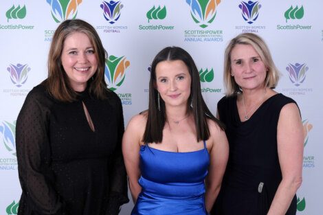 Three women posing for a photo in front of a green wall.