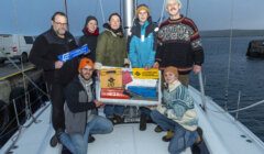 A group of people standing on a boat holding a box.