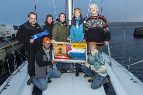 A group of people standing on a boat holding a box.