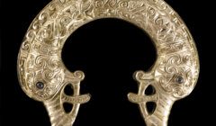 A gold brooch with an ornate design on it.