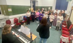 A group of people singing in a room with a piano.