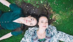 Two women laying on the grass with their hair down.