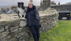 A woman with a dog standing next to a stone wall.