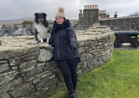 A woman with a dog standing next to a stone wall.