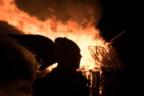 A silhouette of a person standing in front of a fire.