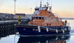 A blue and orange lifeboat is docked at a pier.