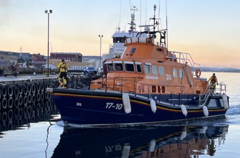 A blue and orange lifeboat is docked at a pier.