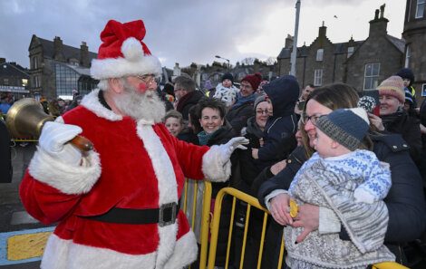 Santa claus greeting a child in front of a crowd.