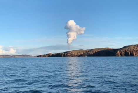 A cloud of smoke is coming out of a body of water.