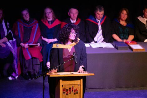 A woman in a graduation gown standing at a podium.