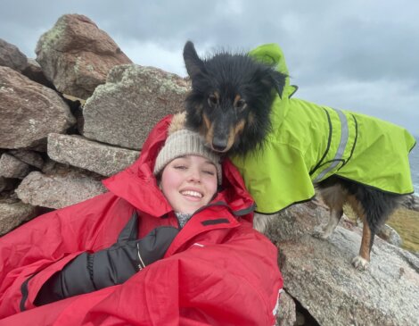 A woman in a red raincoat with a dog on a rock.