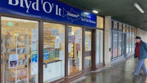 A man walks past a shop with a sign on it.