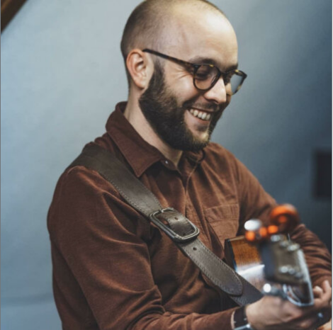 A man smiling while playing an acoustic guitar.