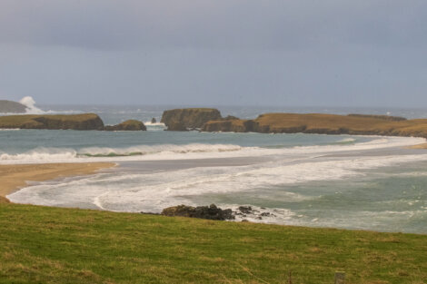 A beach with waves and cliffs in the background.