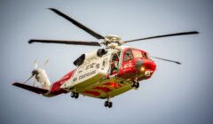 A red and white helicopter flying through the sky.