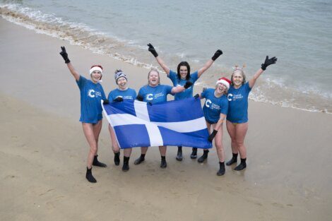 A group of women holding a scottish flag on the beach.