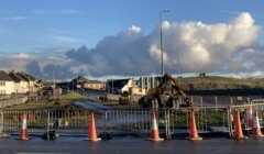 A road with construction cones and a cloudy sky.