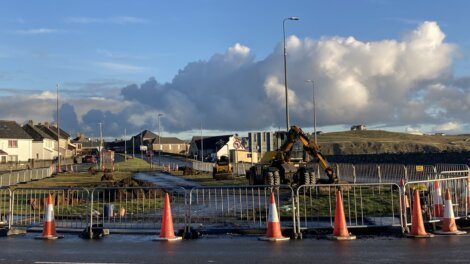 A road with construction cones and a cloudy sky.