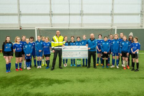 A group of soccer players posing with a cheque.