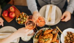 A group of people toasting wine glasses at a thanksgiving dinner table.