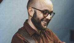 A bearded man smiling while playing an acoustic guitar.