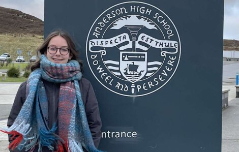 A woman in a scarf standing in front of a sign.