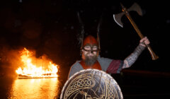 A man holding an axe in front of a fire.