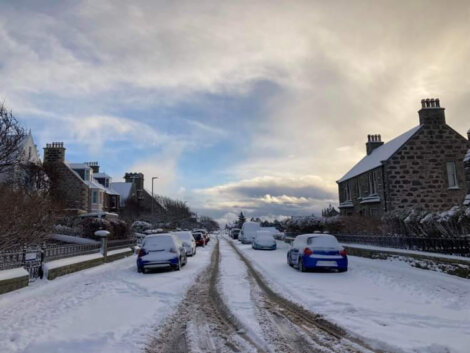 A street covered in snow with cars parked on it.