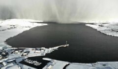 An aerial view of a snow covered lake with a boat in the background.