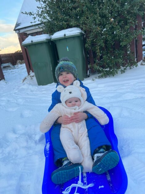 Two children sitting on a blue sled in the snow.