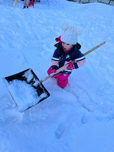 A little girl playing in the snow with a shovel.