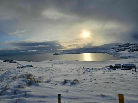 The sun shines over a snow covered field and a body of water.