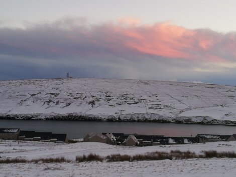 A hill covered in snow with a pink sky.