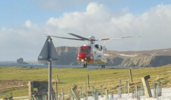 A red and white helicopter flying over a snowy field.