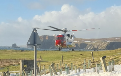 A red and white helicopter flying over a snowy field.