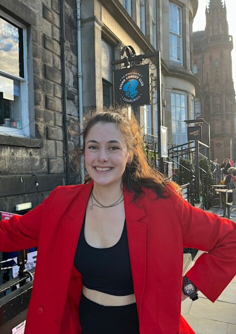 A woman in a red blazer posing in front of a building.