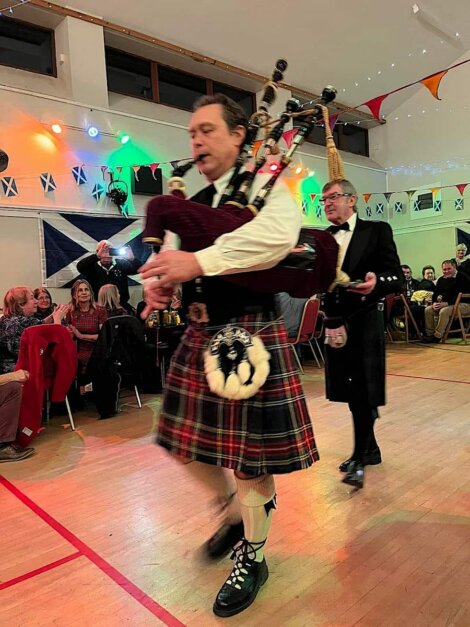 Two men in kilts playing bagpipes in a room.